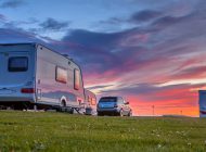 Caravans and cars parked on a grassy campground in summer under beautiful sunset