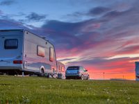 Caravans and cars parked on a grassy campground in summer under beautiful sunset