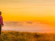 Young hikers standing beside their dome tent pitched high on a grassy mountain ridge looking over the clouds to the golden sunset beyond. ProPhoto RGB profile for maximum color fidelity and gamut.
